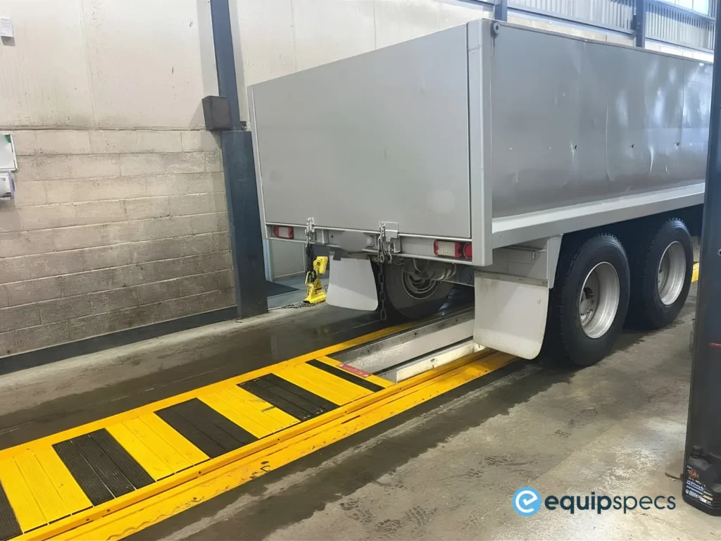 Heavy vehicle trailer positioned above an automatic pit cover system in a commercial workshop inspection lane.